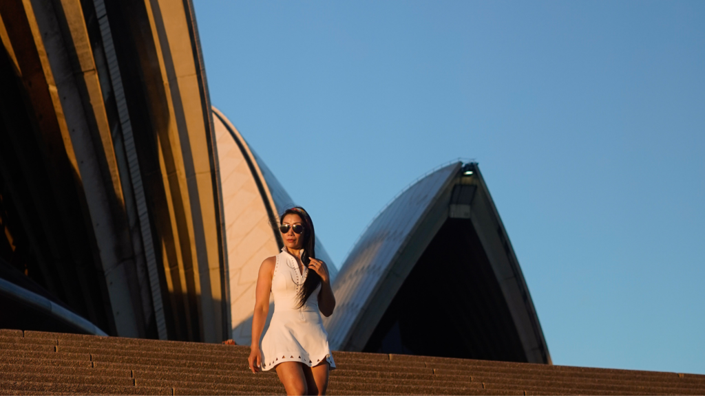 Woman standing on Sydney Opera House steps during sunset, representing strength and transition during midlife